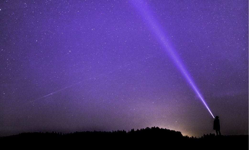 Eine Person Leuchtet mit einer Taschenlampe in den lilanen Nachthimmel