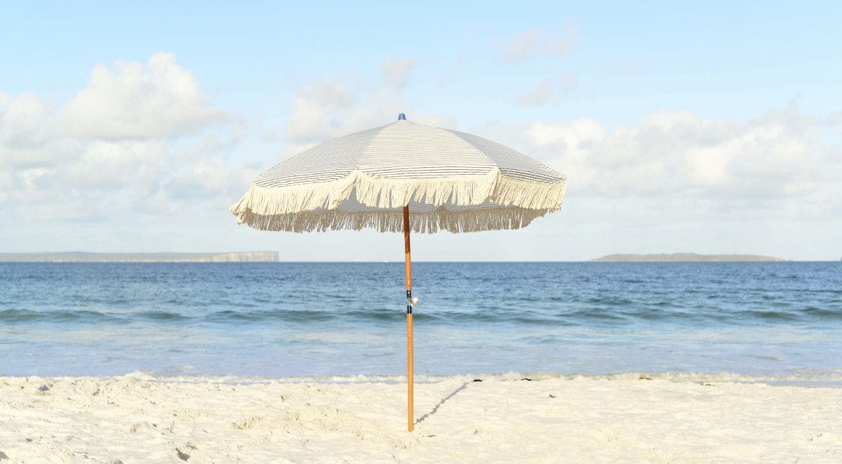 Ein einzelner weißer Sonnenschirm steht an einem Sandstrand. Das Meer und der Himmel sind blau.
