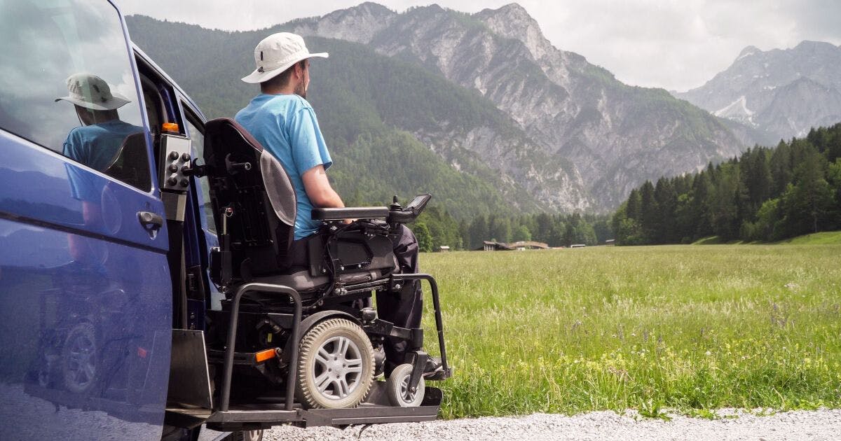 Reisen mit Elektro Rollstuhl - Rollstuhlrampe eines Campers. Im Hintergrund Berge und eine Bergwiese.
