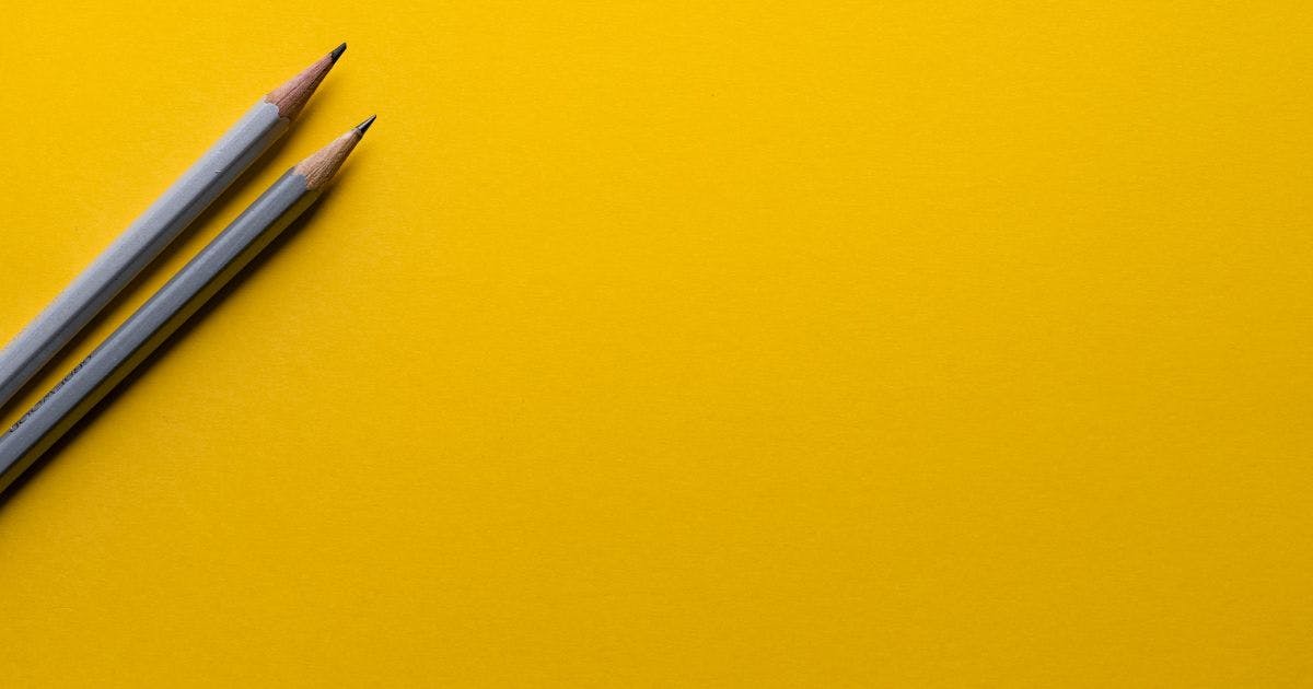 Auf dem Bild befinden sich zwei graue Bleistifte auf gelbem Grund. Die Stifte liegen neben einander schräg im Bild.